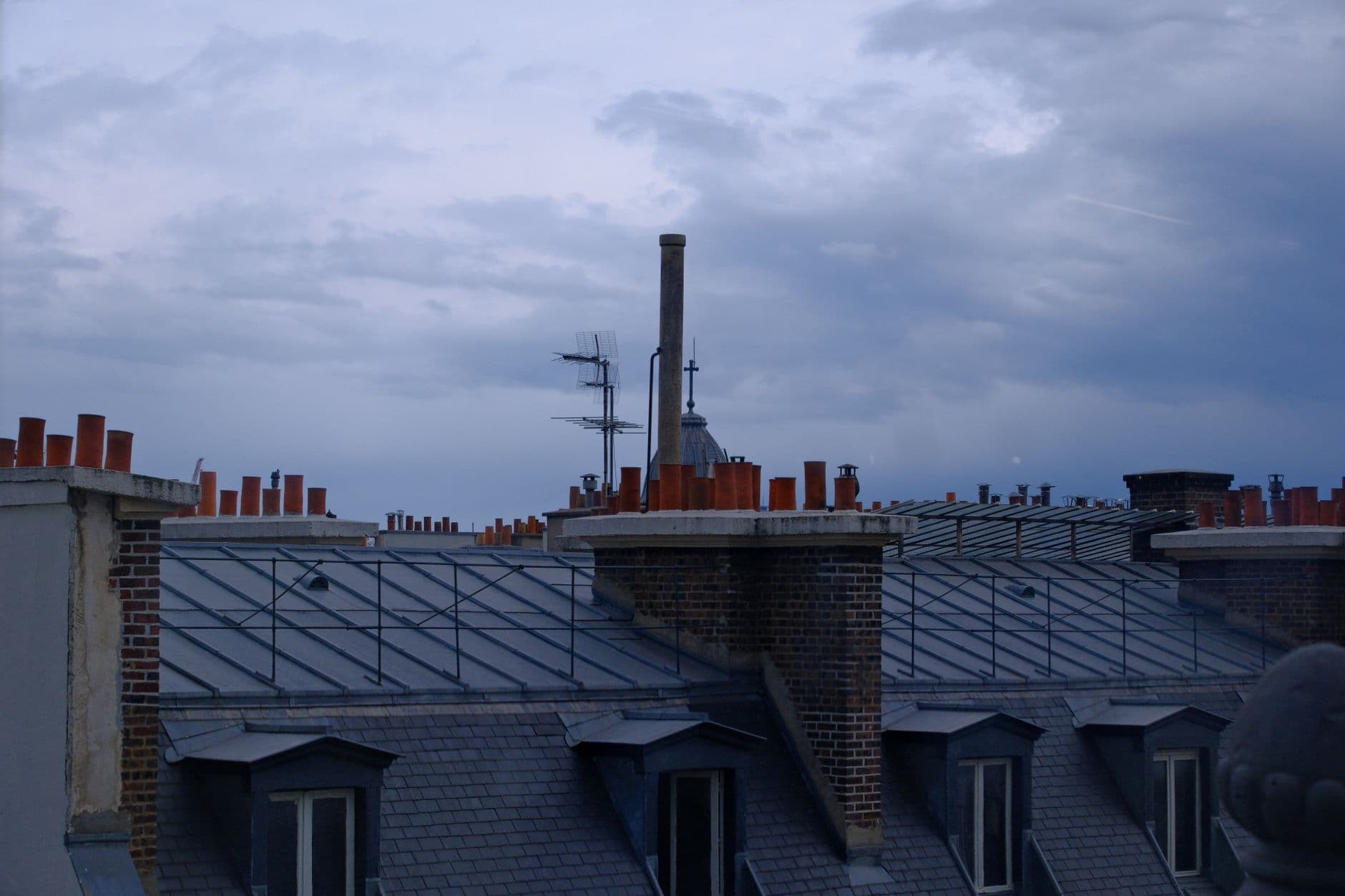 Scenic view of Paris rooftops and chimneys under a cloudy dusk sky.
